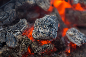 Flame incinerates firewood and transforms it ashes, close up, shallow depth of field. Blaze in a large stove. Nature texture of fire. The flame of fire burns in the brazier, smoldering firewoods.
