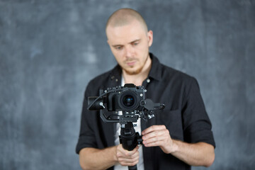 A young professional videographer in a black shirt holds a professional camera on a 3-axis gimbal stabilizer. The cameraman shoots video using a professional movie camera. Stabilization system.