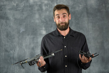 Happy man testing quadcopter. Remote unmanned aerial vehicle with camera. Male holding radio controller. Modern entertainment. Selective focus. A young adult man plays with a quadrocopter and has fun.