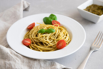 Close-up plate with italian pasta with pesto sauce, garnished with cherry tomatoes and basil leaves.