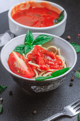 spaghetti with sauce in a plate and tomato sauce with basil in a small bowl with spices seasonings on a black table. copy space, vertical orientation, close up