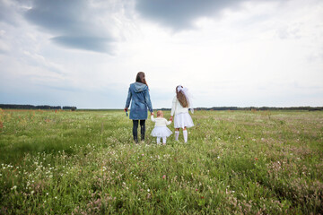 Fototapeta premium A mother with two children walks through a blooming meadow towards the sun-the concept of warm family relations, achieving plans