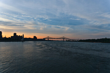 Fototapeta premium A skyline view a steel bridge across a river at the time between sunset and twilight. Jacques Cartier Bridge is across Saint Laurent river. Left is Clock Tower. Right is Saint Helen's Island.