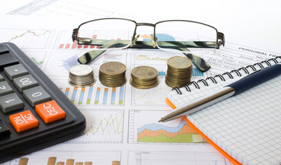 Pen on financial and accounting reports with coins stacks, glasses and calculator in background. Concepts of tax planning and budget management.