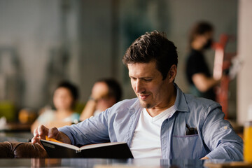 Cheerful handsome successful male sitting in cafe and reading book.