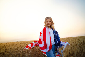 Adorable patriotic girl wearing an American flag in a beautiful wheat field.