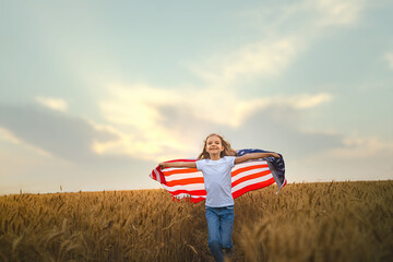 Adorable patriotic girl wearing an American flag in a beautiful wheat field.
