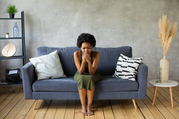 Obraz premium Unhappy African American woman sit on the sofa, the girl is very upset sitting on the couch of her apartment.