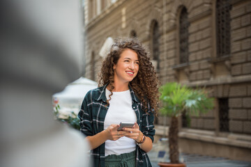 Woman with curly hair holding smart phone and smiling