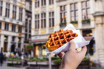 Foto op Plexiglas Man holds waffle with chocolate sauce on the background of city © Katsiaryna