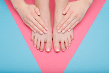 Closeup young well-groomed female foots. Woman doing pedicure and manicure, files nails. Girl applies nail polish. Pink and blue background. Top view. Free space for text.