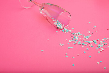 Champagne glass poured out colorful confetti on pink background. Top view. Flat lay. Free space for text.