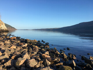 The stunning Loch Ness seen from the rocky shore on a day with the blue sky
