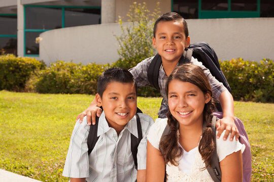 Young Hispanic Student Children Wearing Backpacks On School Campus
