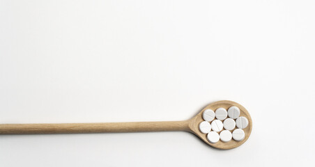Wooden spoon with round tablets on white background isolated. Medications on the table for coronavirus, close up. Free space for text. Pills and drugs. Top view. Banner for web site