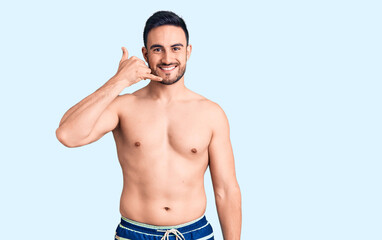 Fototapeta premium Young handsome man wearing swimwear smiling doing phone gesture with hand and fingers like talking on the telephone. communicating concepts.