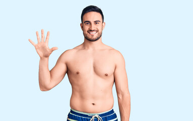 Fototapeta premium Young handsome man wearing swimwear showing and pointing up with fingers number five while smiling confident and happy.