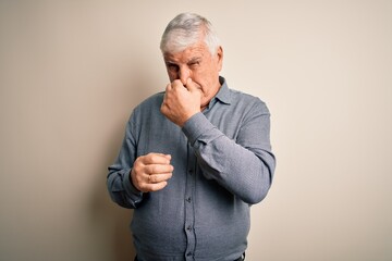 Senior handsome hoary man wearing casual shirt standing over isolated white background smelling...