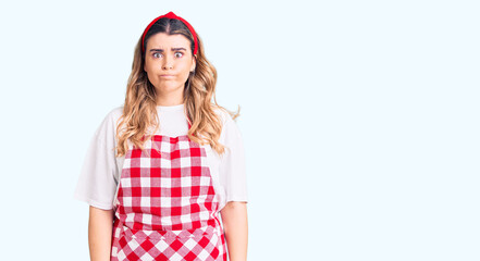 Young caucasian woman wearing apron puffing cheeks with funny face. mouth inflated with air, crazy expression.