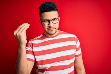 Young handsome man wearing casual striped t-shirt and glasses over isolated red background Doing Italian gesture with hand and fingers confident expression