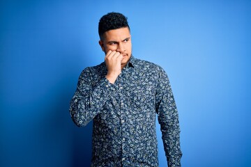 Young handsome man wearing casual shirt standing over isolated blue background looking stressed and nervous with hands on mouth biting nails. Anxiety problem.
