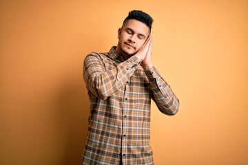 Young handsome man wearing casual shirt standing over isolated yellow background sleeping tired dreaming and posing with hands together while smiling with closed eyes.