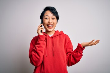 Young beautiful asian girl having conversation talking on the smartphone over white background very happy and excited, winner expression celebrating victory screaming with big smile and raised hands