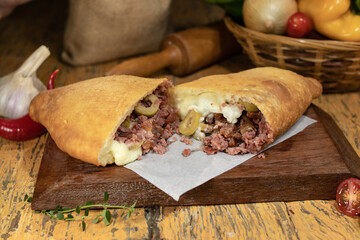 Fogazza stuffed with minced meat and curd, creamy cheese, catupiry cheese on wooden table with decorated blurred background