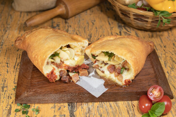 Fogazza stuffed with mozzarella, champignon mushroom, bacon, sun-dried tomatoes and mangering on wooden table with decorated blurred background