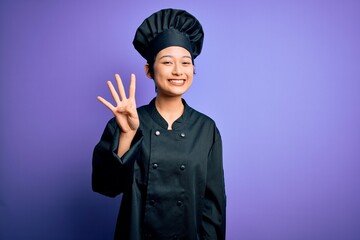 Young beautiful chinese chef woman wearing cooker uniform and hat over purple background showing and pointing up with fingers number four while smiling confident and happy.