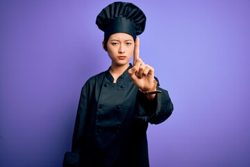 Young beautiful chinese chef woman wearing cooker uniform and hat over purple background Pointing with finger up and angry expression, showing no gesture