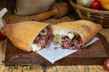 Fogazza stuffed with minced meat and curd, creamy cheese, catupiry cheese on wooden table with decorated blurred background