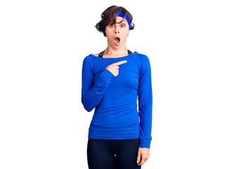 Beautiful young woman with short hair wearing training workout clothes surprised pointing with finger to the side, open mouth amazed expression.