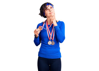 Beautiful young woman with short hair wearing winner medals serious face thinking about question with hand on chin, thoughtful about confusing idea