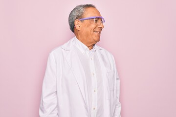 Senior grey-haired scientist man wearing glasses and coat over isolated pink background looking...