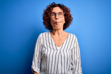 Fototapeta na wymiar Middle age beautiful curly hair woman wearing casual striped shirt over isolated background making fish face with lips, crazy and comical gesture. Funny expression.