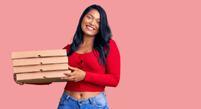 Hispanic woman with long hair holding delivery pizza box looking positive and happy standing and smiling with a confident smile showing teeth