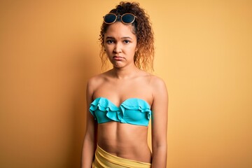 Young beautiful american woman on vacation wearing bikini over isolated yellow background Relaxed with serious expression on face. Simple and natural looking at the camera.