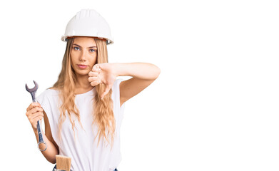 Beautiful caucasian woman with blonde hair wearing hardhat and builder clothes with angry face, negative sign showing dislike with thumbs down, rejection concept