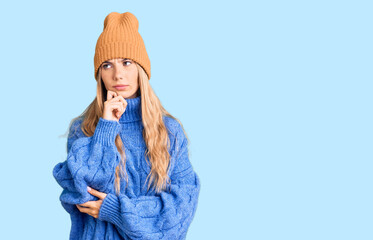 Beautiful caucasian woman with blonde hair wearing wool sweater and winter hat serious face...