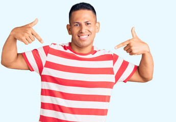 Young handsome latin man wearing casual clothes looking confident with smile on face, pointing...