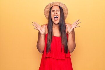 Young beautiful brunette woman wearing summer hat and dress celebrating mad and crazy for success with arms raised and closed eyes screaming excited. winner concept