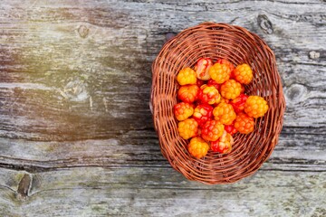 Handful of Cloudberry in wooden basket on an old wooden board background. Healthy diet. Collecting forest ripe cloudberries from the forest. Summer berry. View from the top with flare light