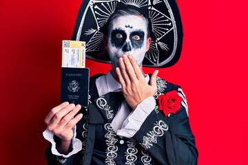 Young man wearing mexican day of the dead costume holding united states passport and boarding pass covering mouth with hand, shocked and afraid for mistake. surprised expression