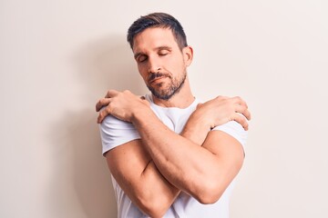 Young handsome man wearing casual t-shirt standing over isolated white background hugging oneself...