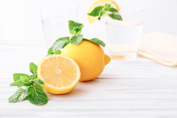 Lemon and mint leaves on wooden table and glasses of water on light background