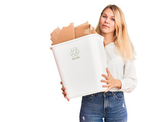 Young beautiful blonde woman holding recycle paper bin thinking attitude and sober expression looking self confident