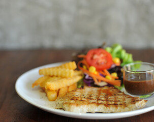 plate of grilled pork steak with french fries and salad on wood background
