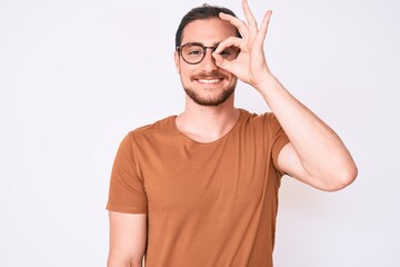 Young handsome man wearing casual clothes and glasses smiling happy doing ok sign with hand on eye looking through fingers