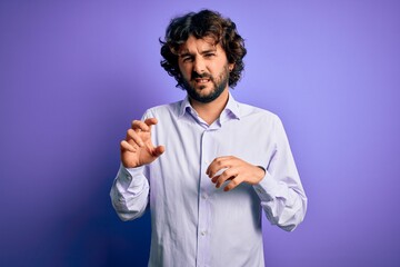 Young handsome business man with beard wearing shirt standing over purple background disgusted expression, displeased and fearful doing disgust face because aversion reaction.